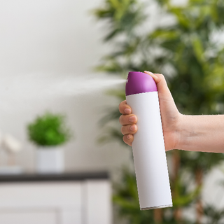 Hand som håller en vit och lila sprayflaska, med produkten som sprutas ut i luften.