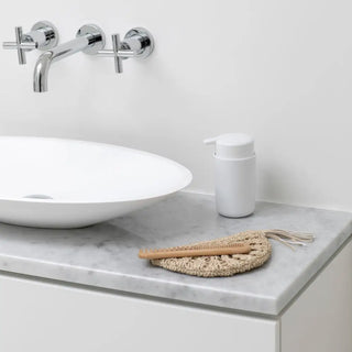 Vitt badrumshandfat i keramik med en väggmonterad kran i krom.