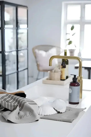 Randig diskhandduk och städprodukter vid kökssin, inklusive rengöringsmedel