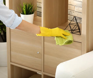 Hand i gul handske torkar av en trähylla med en grön trasa.