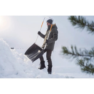 Man i vinterkläder med snöskovel för Fiskars SnowXpert™ Snösläde