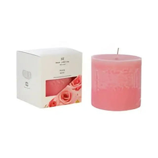 Ett cylindriskt rosa pelarljus med doft av ros, tillsammans med en dekorativ ask.